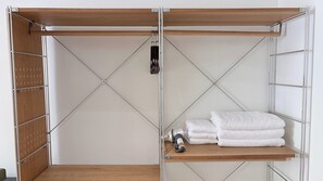 A room with a wooden wardrobe, a metal shelf with towels, and a camera on the shelf. - Brown H (Bangkok)