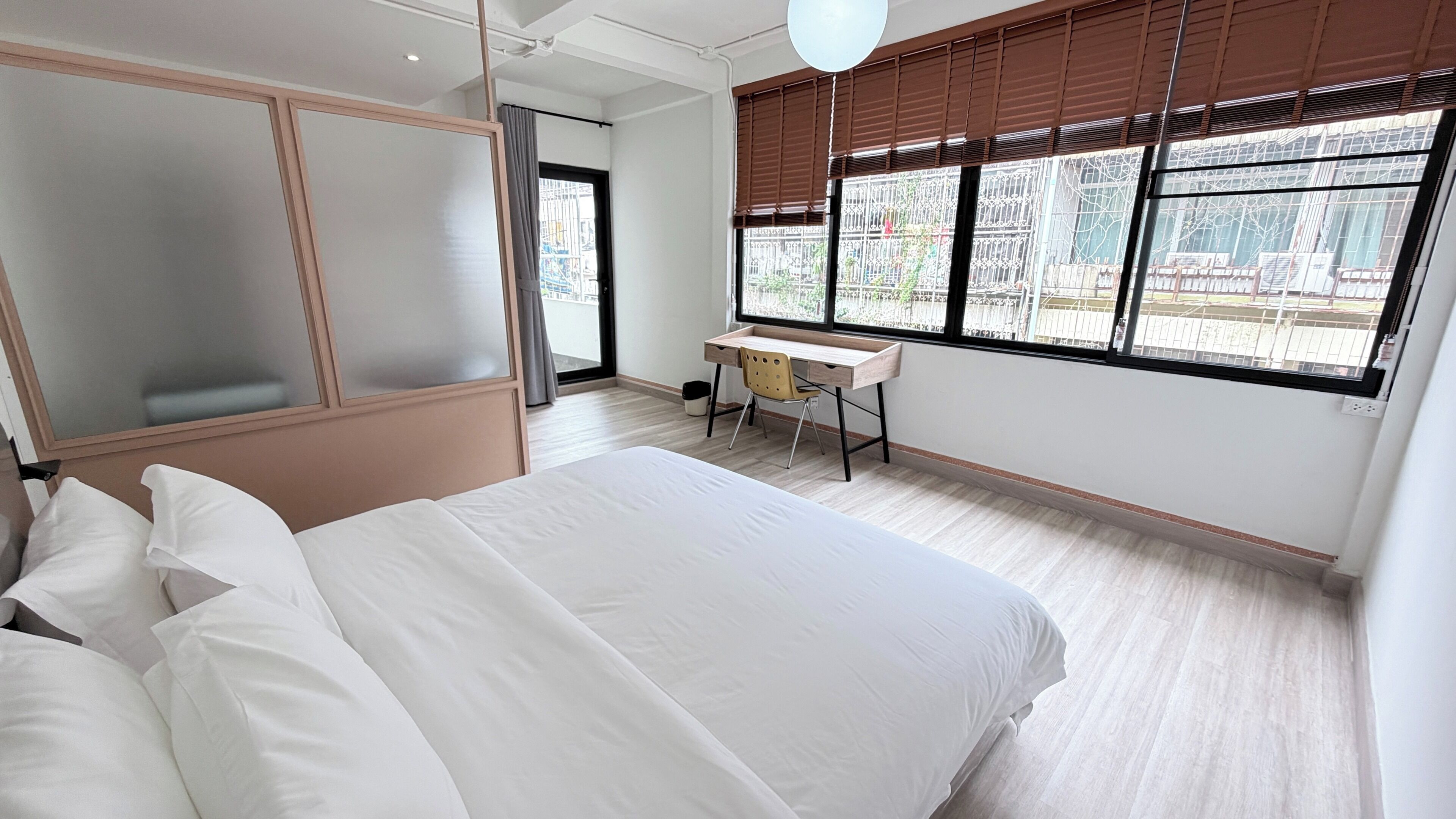 A hotel room with a bed, a desk, and a window with blinds.