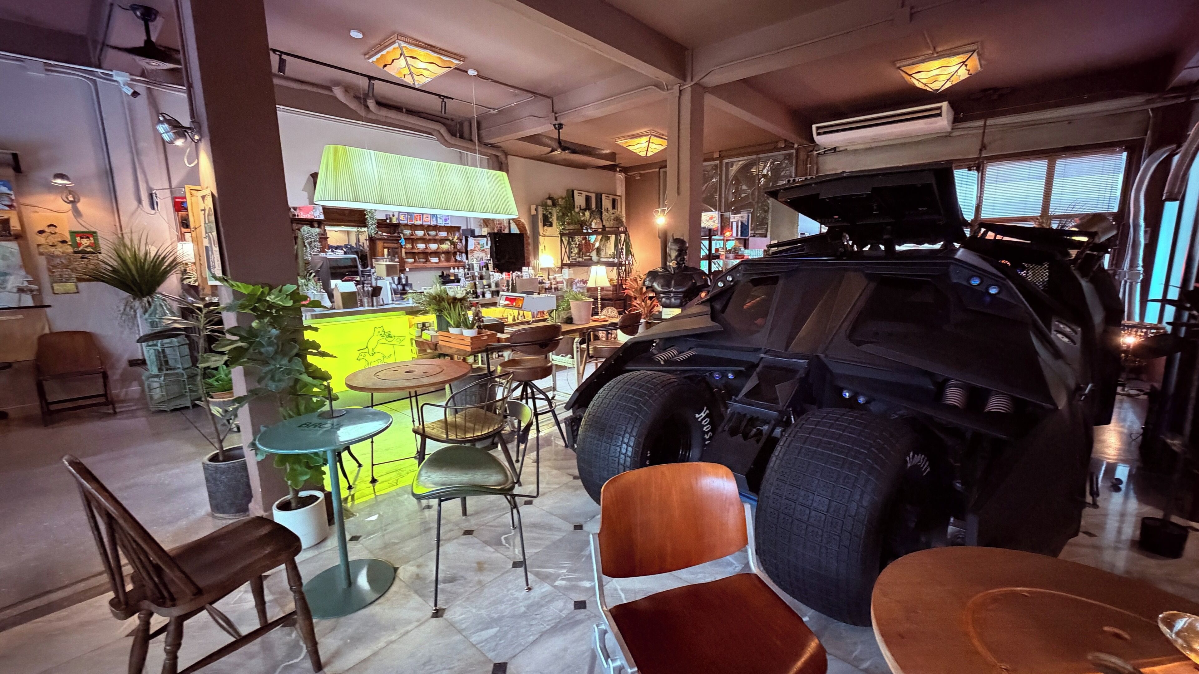 A room with a large vehicle, chairs, tables, and a bar area.