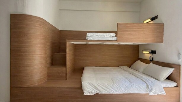 A compact, modern bedroom with a curved wooden headboard, a bunk bed, and a bedside table with a lamp. - Brown H (Bangkok)
