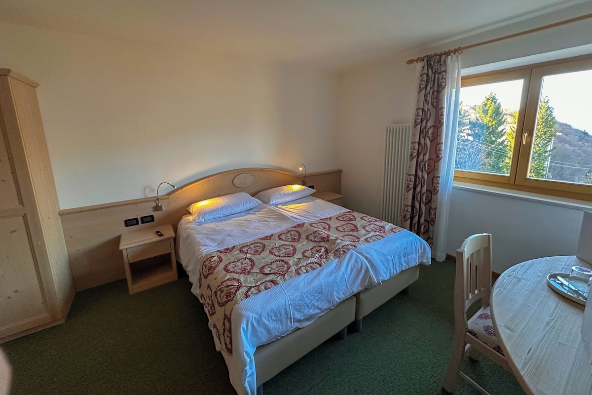 A bedroom with a bed, bedside table, lamp, chair, and a window with a view of trees.