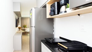 A modern kitchen with a built-in refrigerator, a coffee machine, and a microwave on a wooden shelf.