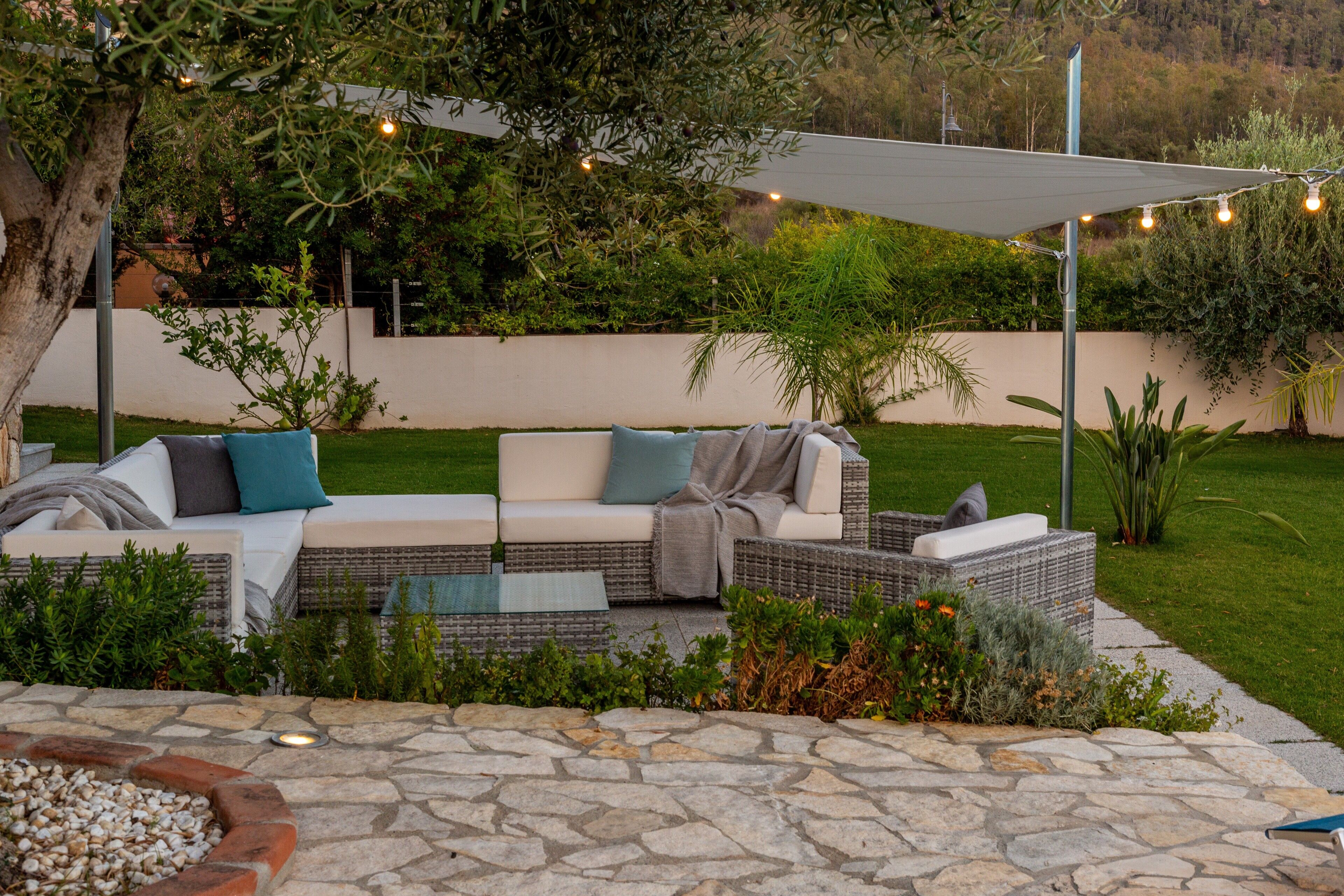 An outdoor seating area with a stone patio, a white sofa with cushions, and a pergola with string lights.