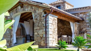 Un edificio de piedra con un patio techado, mobiliario exterior y una pequeña piscina.