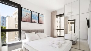 Habitación de hotel moderna con una cama grande, una mesita de noche, un espejo y vistas a la ciudad.