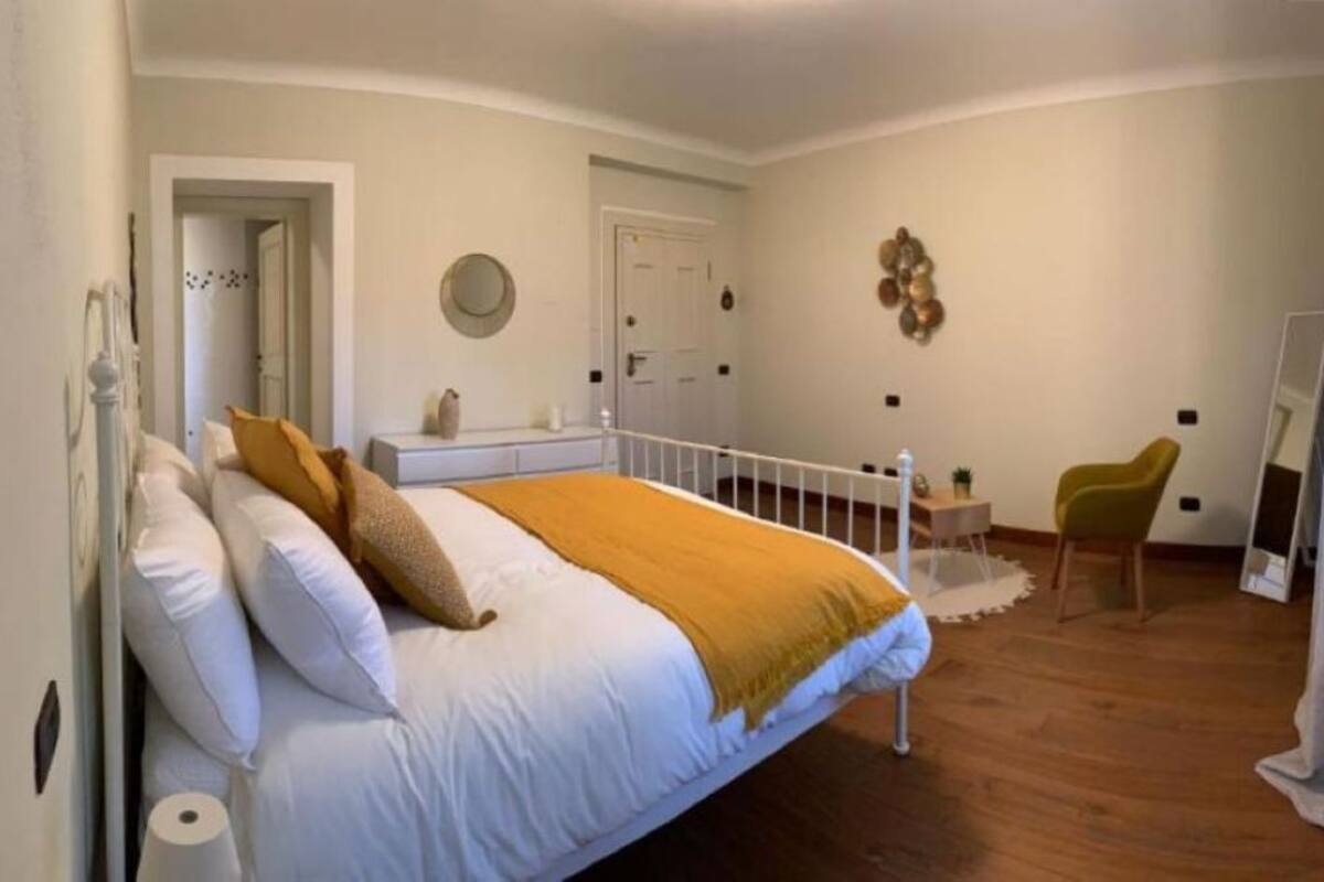 A bedroom with a bed, a chair, a mirror, and a door.