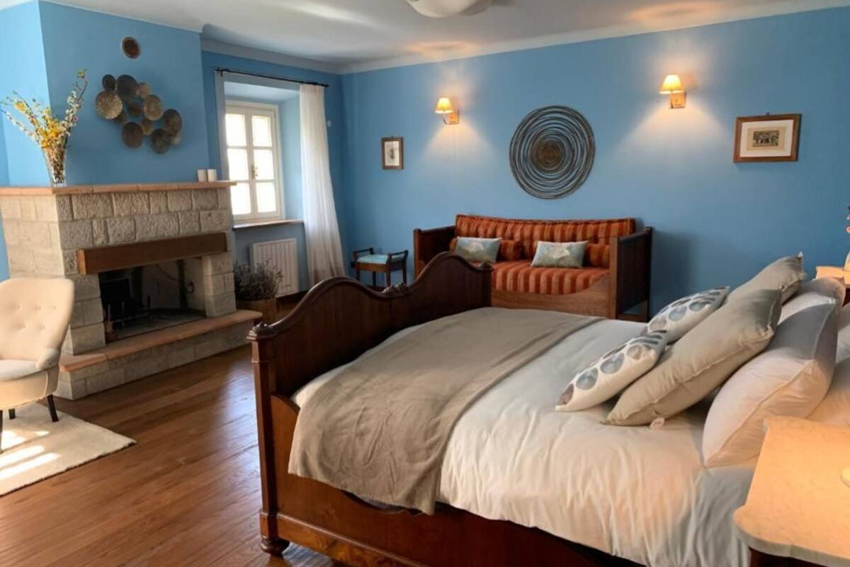 A bedroom with a large bed, a fireplace, a sofa, and a chair.