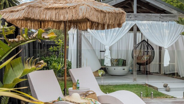 A poolside area with lounge chairs, a hanging chair, a thatched umbrella, and a white building with curtains. - Bahagia Oasis - 4pm check out Sundays* (Safety Beach)