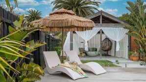A poolside area with lounge chairs, a thatched umbrella, and a covered seating area with white curtains. - Bahagia Oasis - 4pm check out Sundays* (Safety Beach)