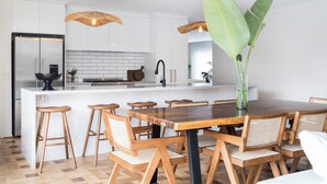 A modern kitchen with white cabinets, a central island with stools, and a dining table with chairs. - Bahagia Oasis - 4pm check out Sundays* (Safety Beach)