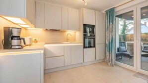 Une cuisine moderne dotée d’appareils électroménagers intégrés, un coin repas avec vue et une porte-fenêtre coulissante donnant sur l’extérieur.