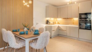 Une cuisine moderne avec des meubles blancs, une table à manger en bois, des chaises confortables et un four encastré.