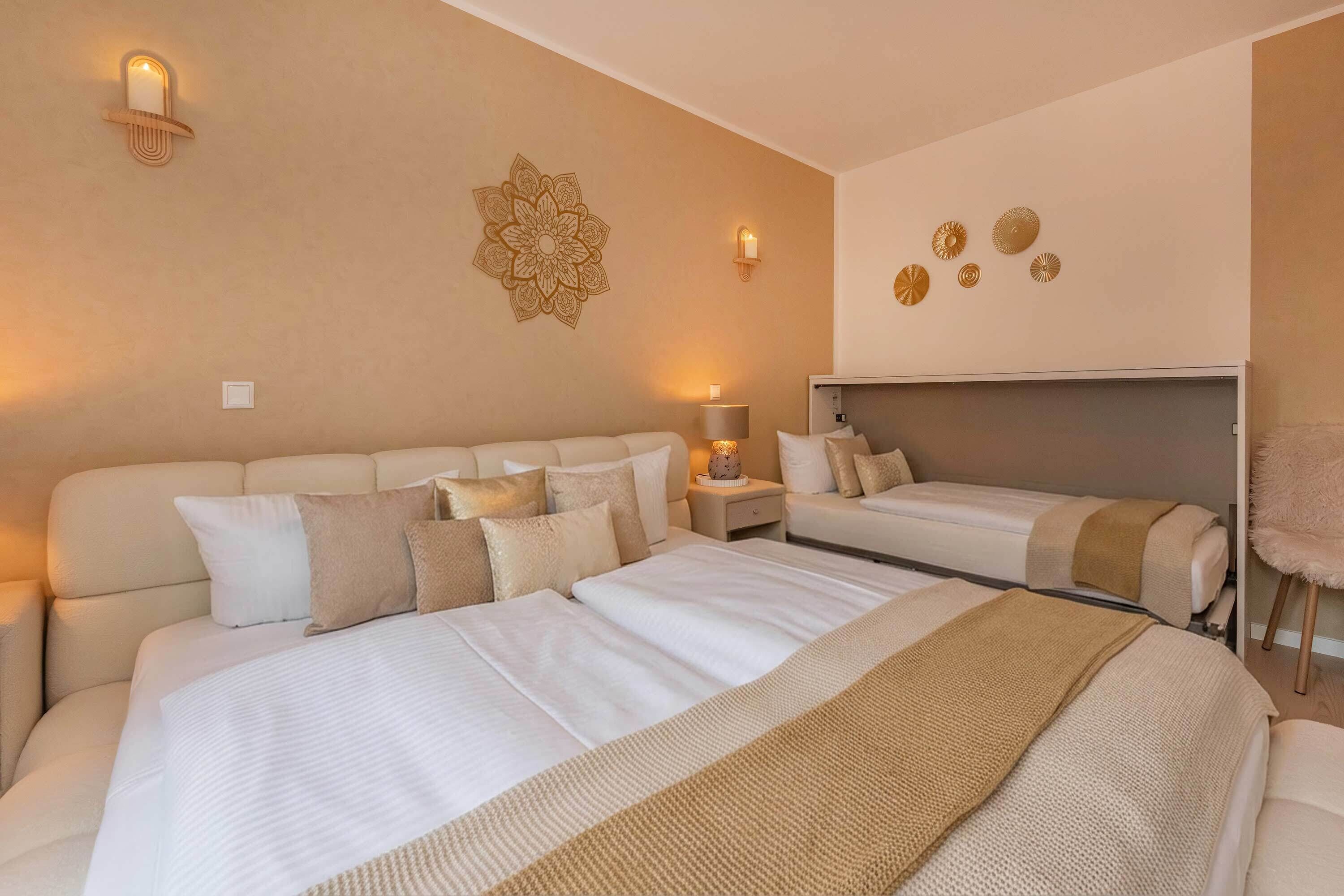 Habitación de hotel con una cama grande, una cama más pequeña, una mesita de noche con lámpara, un adorno en la pared y un ventilador de techo.