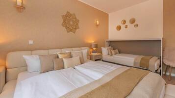Habitación de hotel con una cama grande, una cama más pequeña, una mesita de noche con lámpara, un adorno en la pared y un ventilador de techo.