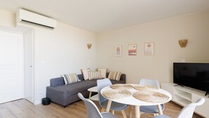 A modern living room with a gray sofa, a round dining table with woven placemats, and a flat-screen TV on a white stand. - Superb T2 with Port view Antibes Residence standing Clim Private Parking Wi-Fi (Antibes)