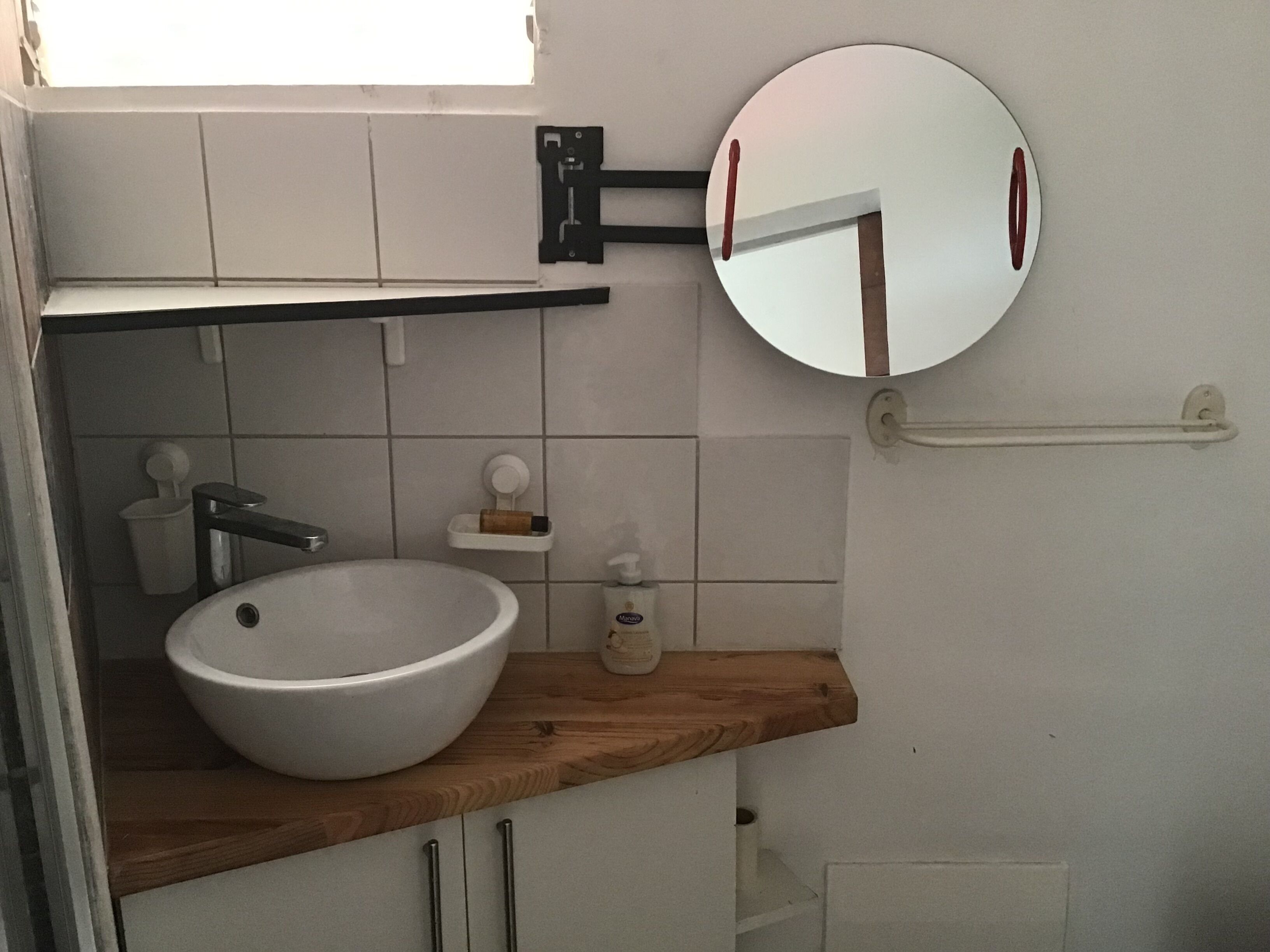 Ein Badezimmer mit einem weißen Waschbecken, einer Holzausziehtafel, einem Spiegel und einem Handtuchhalter.