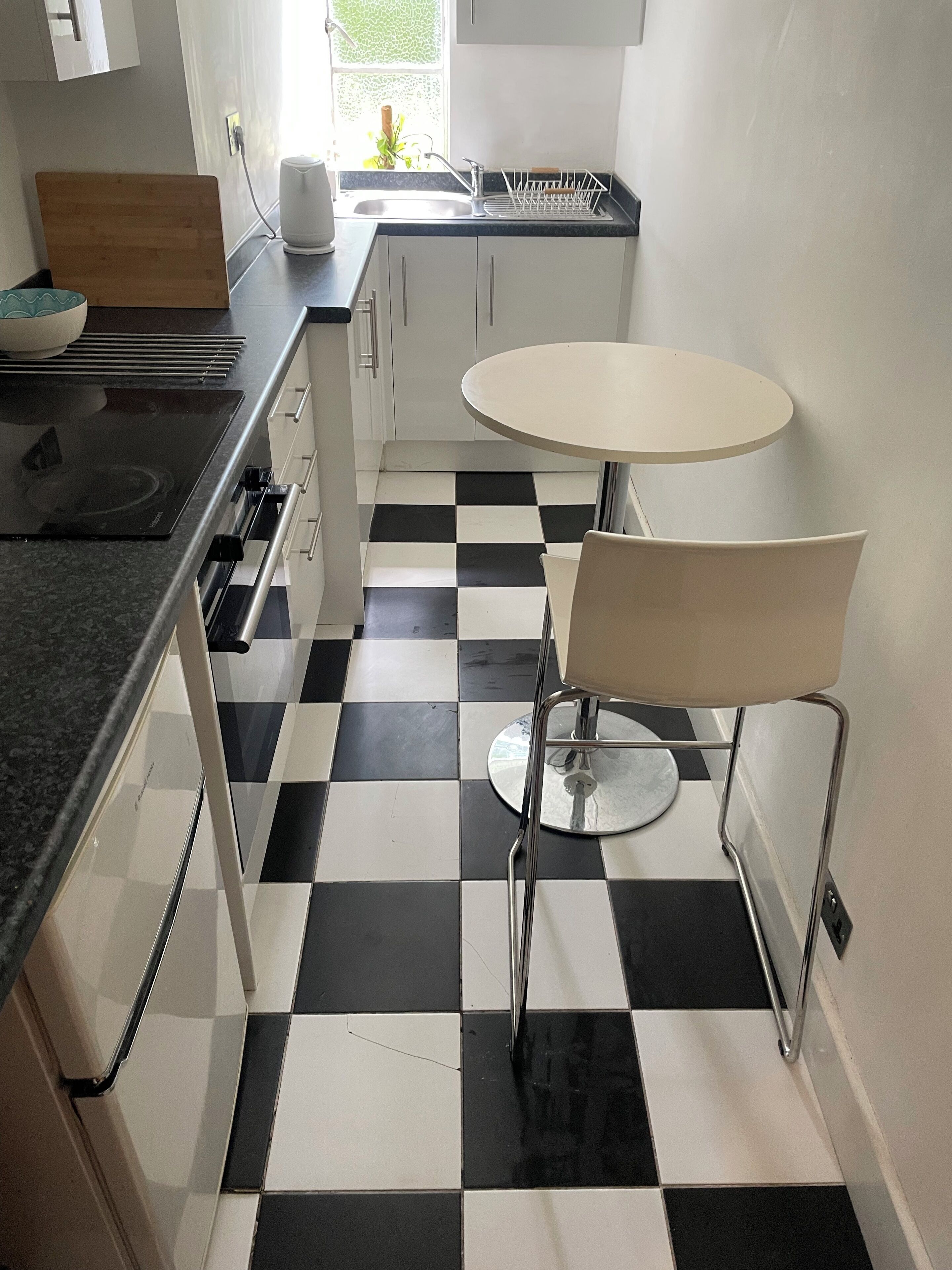 Een keuken met een geruit vloertje, een witte tafel met een stoel, en een inbouwoven.