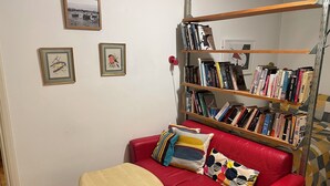 A cozy room with a red leather sofa, a wooden bookshelf filled with books, and two framed pictures on the wall. - Artistic, 1930's studio-flat - 20 mins to Central London. (London)