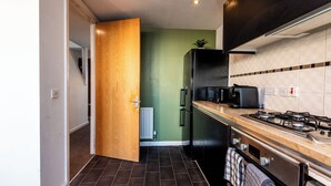 A compact kitchen with a wooden countertop, a gas stove, a black refrigerator, and a microwave. - Family 3 Bedroom House by Guestz (Manchester)