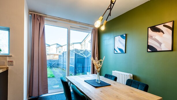 A dining area with a wooden table, black chairs, a vase with dried plants, and a radiator. - Family 3 Bedroom House by Guestz (Manchester)