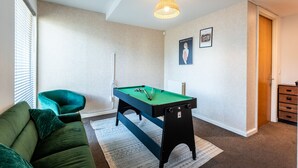 A room with a pool table, a green sofa, a ceiling light, and a door. - Family 3 Bedroom House by Guestz (Manchester)