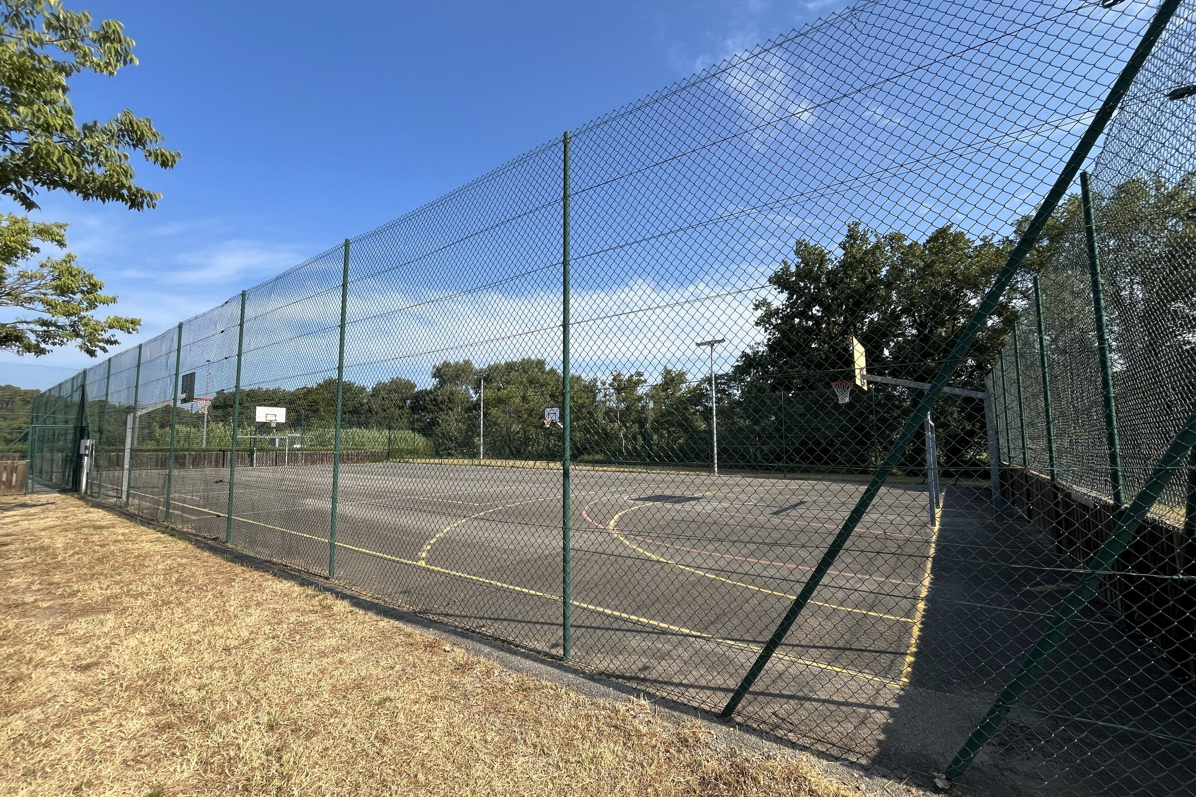 A basketball court enclosed by a chain-link fence with a basketball hoop and a basketball key.