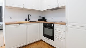 A modern kitchen with white cabinets, a black oven, and a wooden countertop. - RentPlanet - Apartament Chmielna (Warsaw)