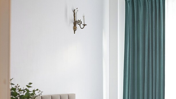 A neatly arranged hotel room with a bed, a chair, a small table, and a wall-mounted light fixture. - RentPlanet - Apartament Chmielna (Warsaw)
