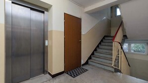A hallway with a metallic elevator, a wooden door, and a staircase with a red handrail. - Cozy Studio in the Center | Workspace (Gdynia)