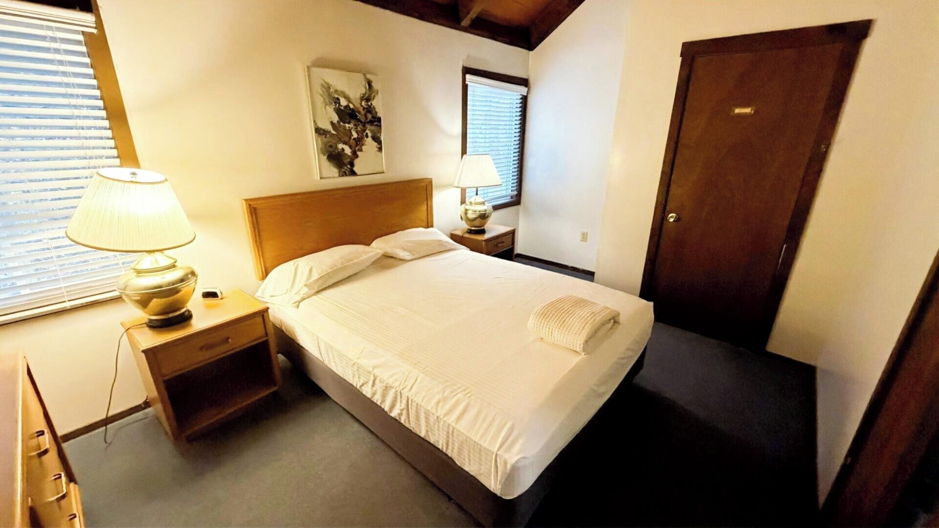 A bedroom with a bed, nightstands, a lamp, a painting, and a door.