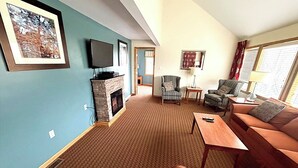 A living room with a fireplace, a television, and two armchairs. - Mountain Fun for Everyone – 3BR Tri-Level Condo Near Bryce Resort (Basye)