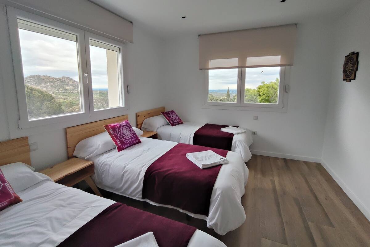 A hotel room with three beds, large windows, and a view of the landscape.