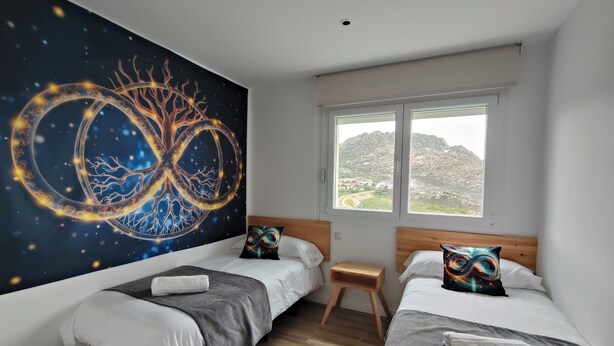 Ein Schlafzimmer mit zwei Betten, einem großen Wandbild, einem Fenster mit Blick auf eine Berglandschaft und einem kleinen Holzschemel.