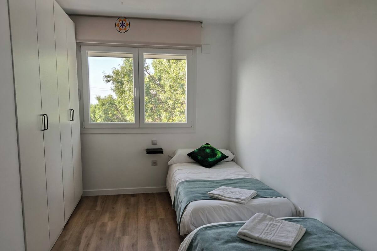 A bedroom with a single bed, a wardrobe, a window, and a small bedside table.