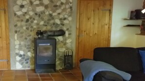 A room with a stone wall, a wood-burning stove, a black sofa, and a tiled floor. - "Kerrin" by Interhome (Aars)