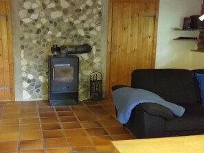 A room with a stone wall, a wood-burning stove, a black sofa, and a tiled floor. - "Kerrin" by Interhome (Aars)