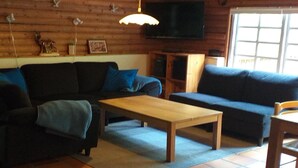 A log cabin interior with a sofa, a coffee table, a TV, and a window. - "Kerrin" by Interhome (Aars)