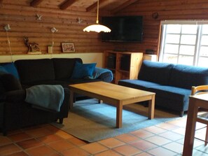 A log cabin interior with a sofa, a coffee table, a TV, and a window. - "Kerrin" by Interhome (Aars)