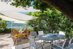 Une terrasse extérieure avec une table ronde, des chaises blanches et un panier de citrons.