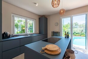 A modern kitchen with a central island, large windows, and a view of a swimming pool. - VILLA OLIVE AND LEMON ESCAPE - A breath between sky and sea, where peace becomes emotion (Rapallo)