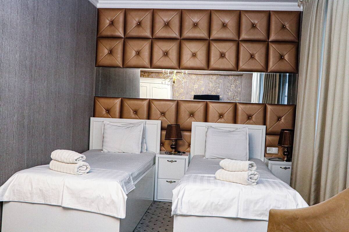 Une chambre d’hôtel avec deux lits, une grande tête de lit rembourrée, un miroir et une table de chevet avec une lampe.
