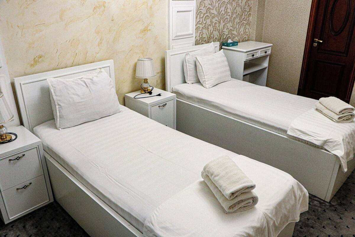 Une chambre d’hôtel avec deux lits simples, une table de chevet avec une lampe, un petit bureau et une armoire.