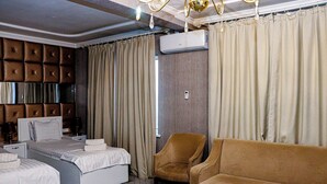 A hotel room with a tufted headboard, two beds, a brown armchair, a sofa, and an air conditioning unit. - Orzu Hotel (Namangan)