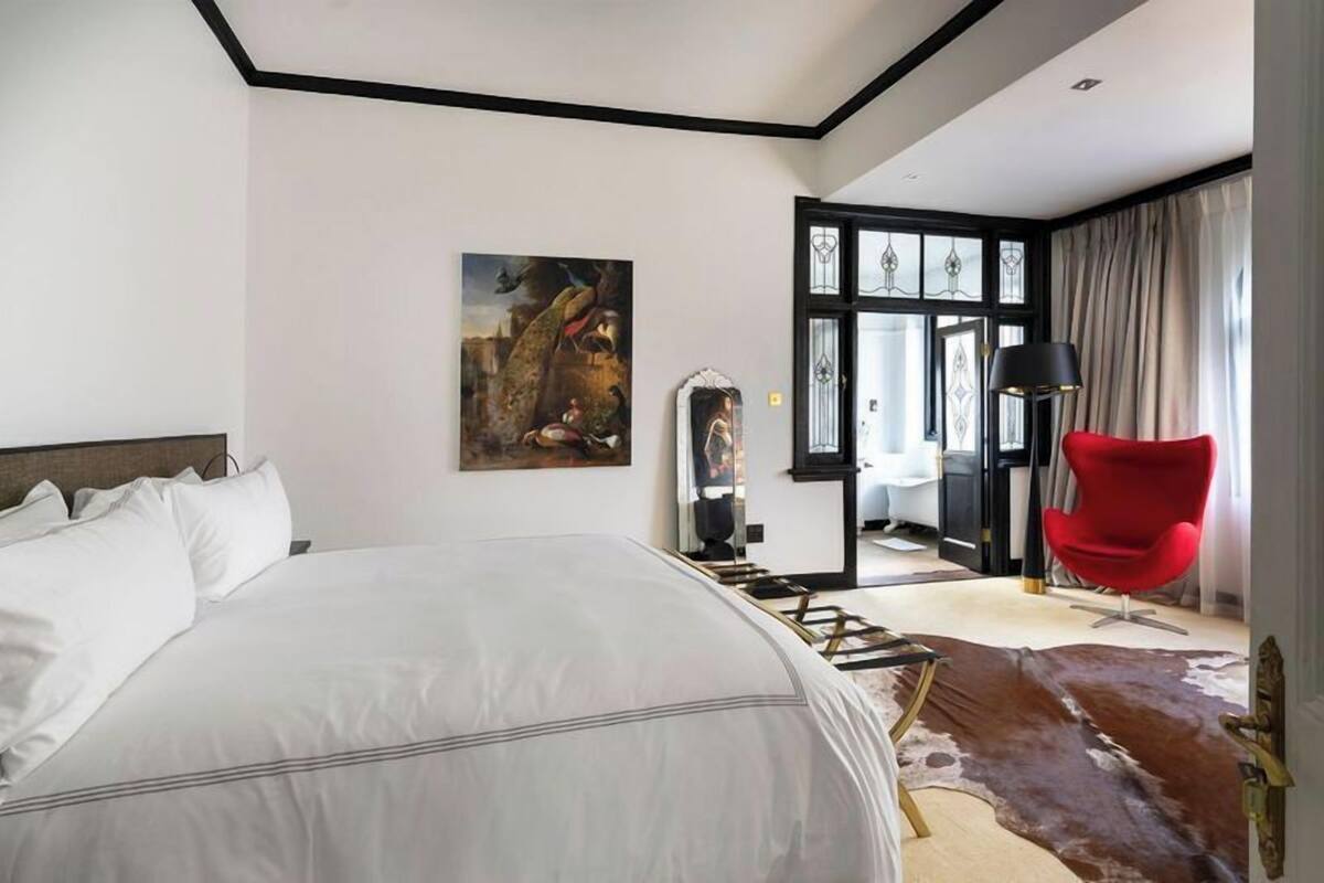 A modern hotel room with a large bed, a red chair, a cowhide rug, and a painting on the wall.