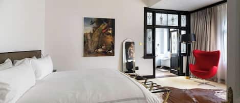 A modern hotel room with a large bed, a red chair, a cowhide rug, and a painting on the wall.
