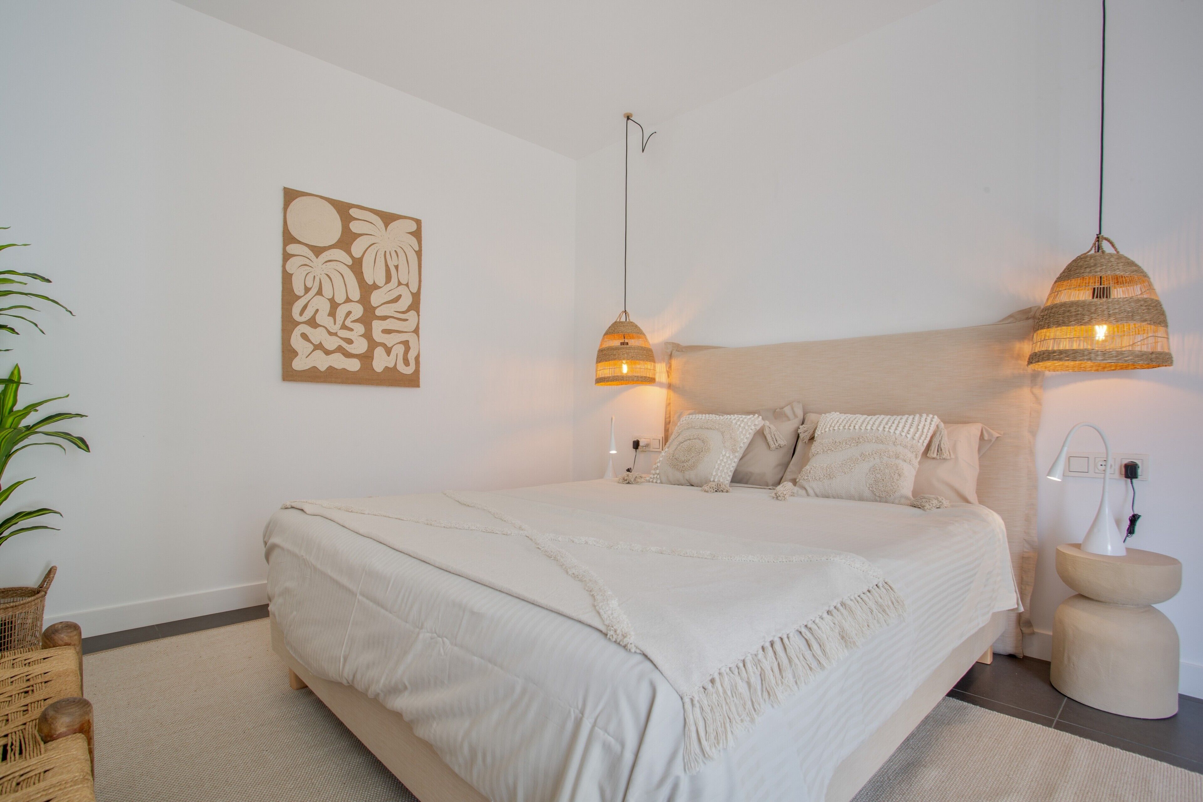 Een slaapkamer met een groot bed, twee hanglampen, een kunstwerk aan de muur en een nachtkastje.