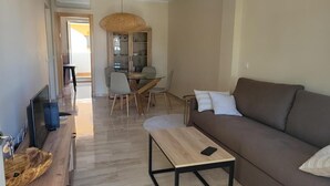 Una sala de estar moderna con un sofá, una mesa de centro, una mesa de comedor con sillas y una televisión.