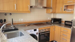 Una cocina con armarios de madera, un lavamanos de acero inoxidable, horno empotrado, microondas y tostadora.