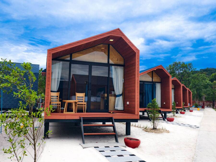 Una hilera de cabañas de madera con ventanas amplias y un espacio de estar al aire libre cubierto.