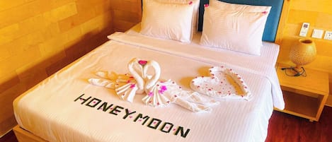 Una habitación de hotel con una cama con cubrecama de temática romántica, un cabecero de madera y una mesita de noche con lámpara.